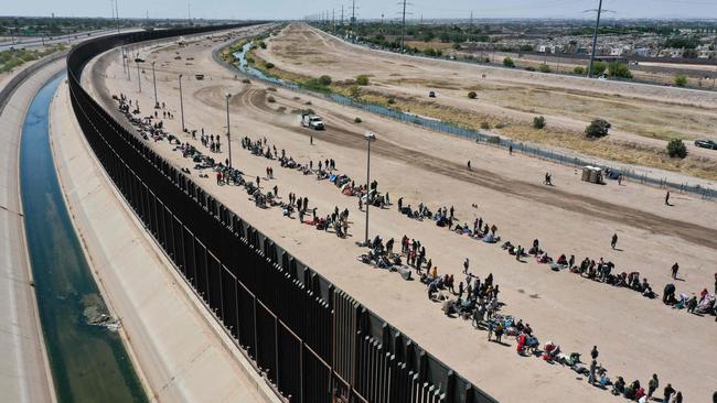 Migrants waiting along the border wall to surrender to US Customs and Border Protection (CBP) border patrol agents for immigration and asylum claim processing after crossing the Rio Grande River into the United States.