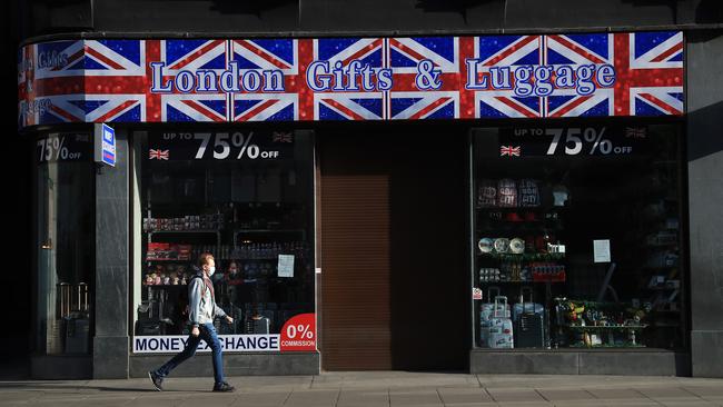 A man wearing a protective mask is seen walking past a closed up gift shop on Oxford Street. Picture: Getty Images