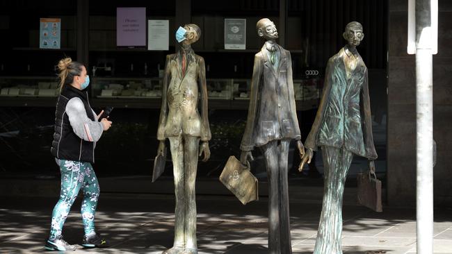 Can’t be too careful: a woman walks past a sensibly masked sculpture at the corner of Swanston and Bourke streets in the empty quarter of central Melbourne. Picture: NCA NewsWire / Andrew Henshaw