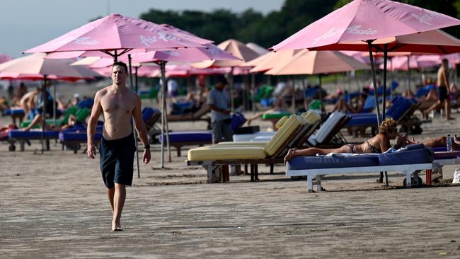 A foreign tourist walks on a beach in Seminyak, Badung regency on Indonesia resort island of Bali, on December 7, 2022. (Photo by SONNY TUMBELAKA / AFP)