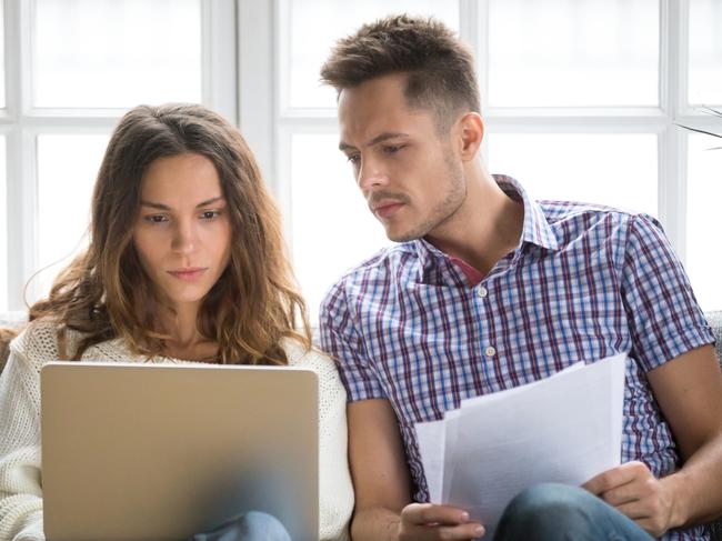 A couple discussing their household bills on the couch including their home loan. Picture: iStock.