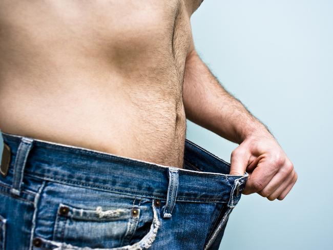 Man stands with an old pair of blue jeans showing his recent weight loss