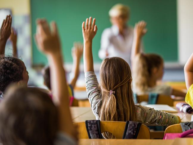 Rear view of large group of students raising their arms to answer the question on a class at elementary school.