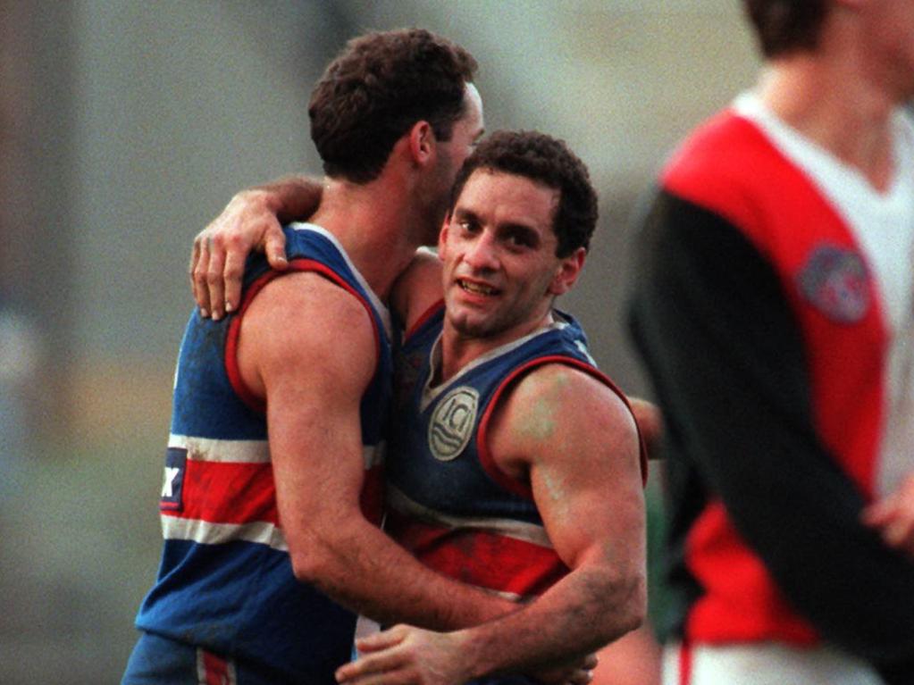 Nigel Kellett and Tony Liberatore embrace during an AFL game in the 1990s. Kellett, now 54, can hardly remember his Brownlow Medal-winning former teammate due to repeated head knocks across his career.