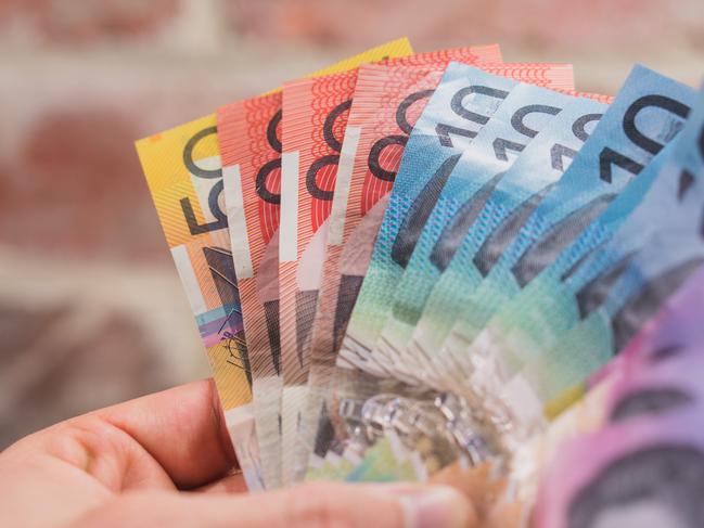 handful of Australian cash with a brick background