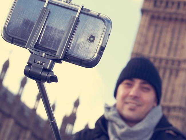 man taking a self-portrait with a selfie stick in front of the Big Ben in London, United Kingdom, with a filter effect