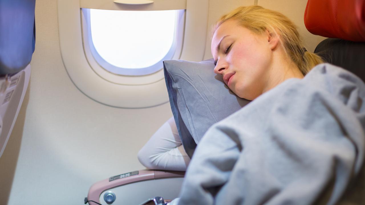 Tired blonde casual caucasian lady napping on uncomfortable seat while traveling by airplane. Commercial transportation by planes.