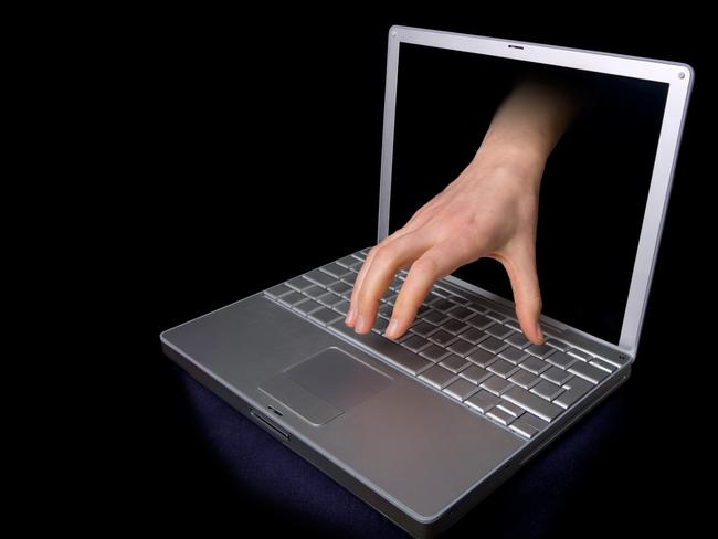 Identity theft, fraud, computer. A hacker concept image of a hand coming through a laptop computer.