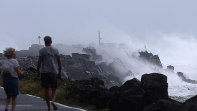 Residents take a morning walk as massive waves crash against the North Wall in Ballina on Wednesday. Picture: AFP