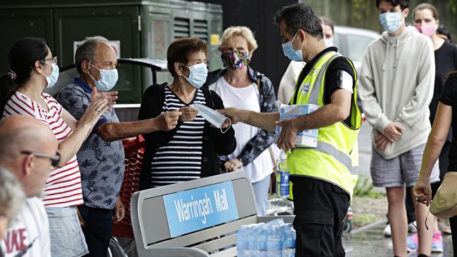 A COVID-19 care team worker hands out water, hand sanitiser and masks to people waiting for tess outside the Brookvale Community Health Centre in northern Sydney on Sunday. Picture: Adam Yip