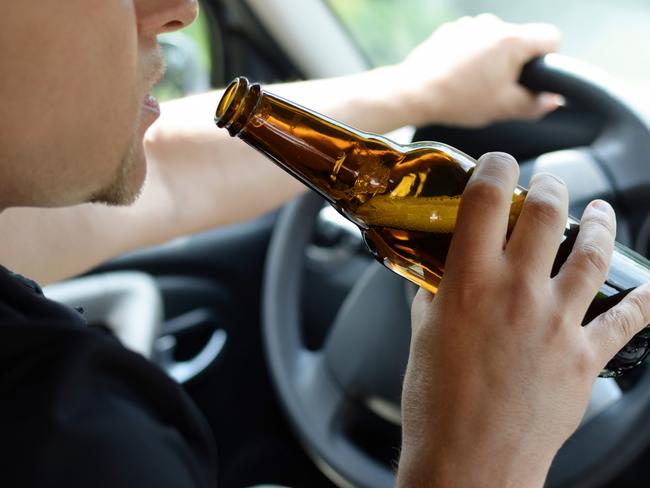 The concept of alcohol driving crime - closeup of young male driver hands with steering wheel and bottle of beer. Drink driving generic. Picture: iSTOCK