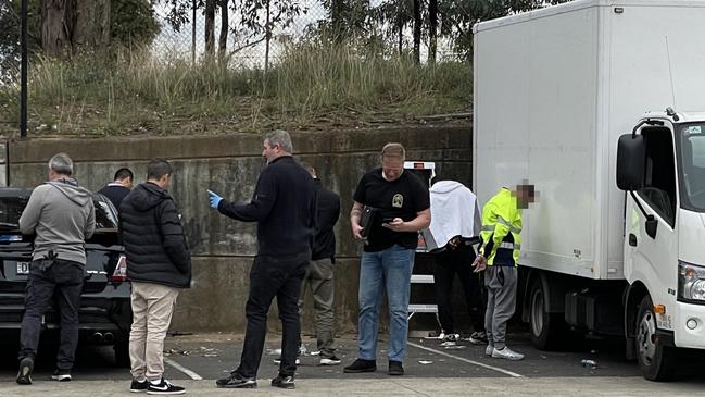 Police operation at Bunnings, Casula, at the Crossroads Homemaker Centre. Four men are in handcuffs, while eyewitnesses reported seeing bags of cash and drugs being taken out of the vehicles. Picture: Paul Brescia