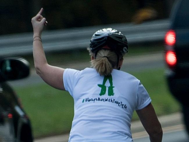 (FILES) This file photo taken on October 28, 2017 shows a woman on a bike gestures with her middle finger as a motorcade with US President Donald Trump departs Trump National Golf Course in Sterling, Virginia. Juli Briskman didn't think twice when she gave President Donald Trump the finger as his motorcade passed her while she was cycling on a road near his golf club. But the obscene gesture, captured on October 28 by AFP White House photographer Brendan Smialowski, who was riding in Trump's convoy, quickly went viral. And it has now cost the single mom her job. / AFP PHOTO / Brendan Smialowski