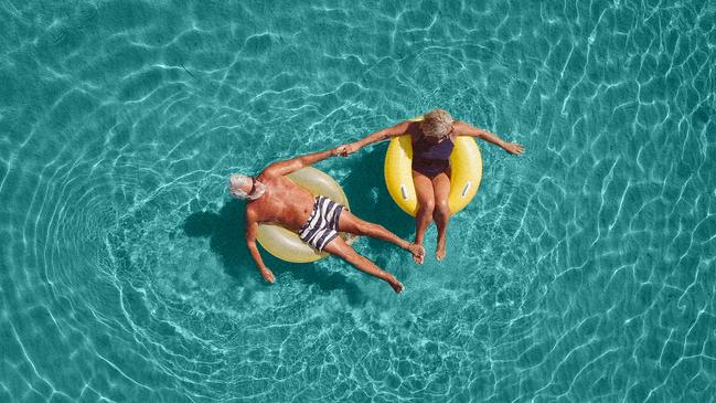 High angle view photo of a senior couple floating in the ocean while using swimming and floating devices; active retirement travel generic