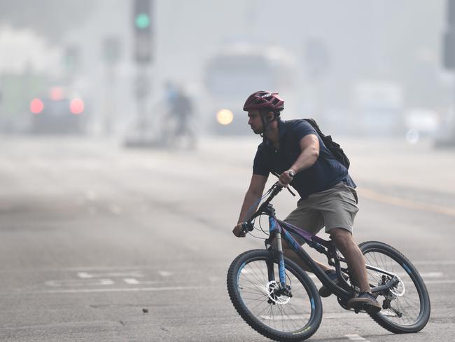 A cyclist is seen through smoke haze from bushfires in Melbourne, Tuesday, January 14, 2020. Smoke haze from the East Gippsland bushfires has drifted across Victoria reaching Melbourne prompting health warnings. (AAP Image/Erik Anderson) NO ARCHIVING