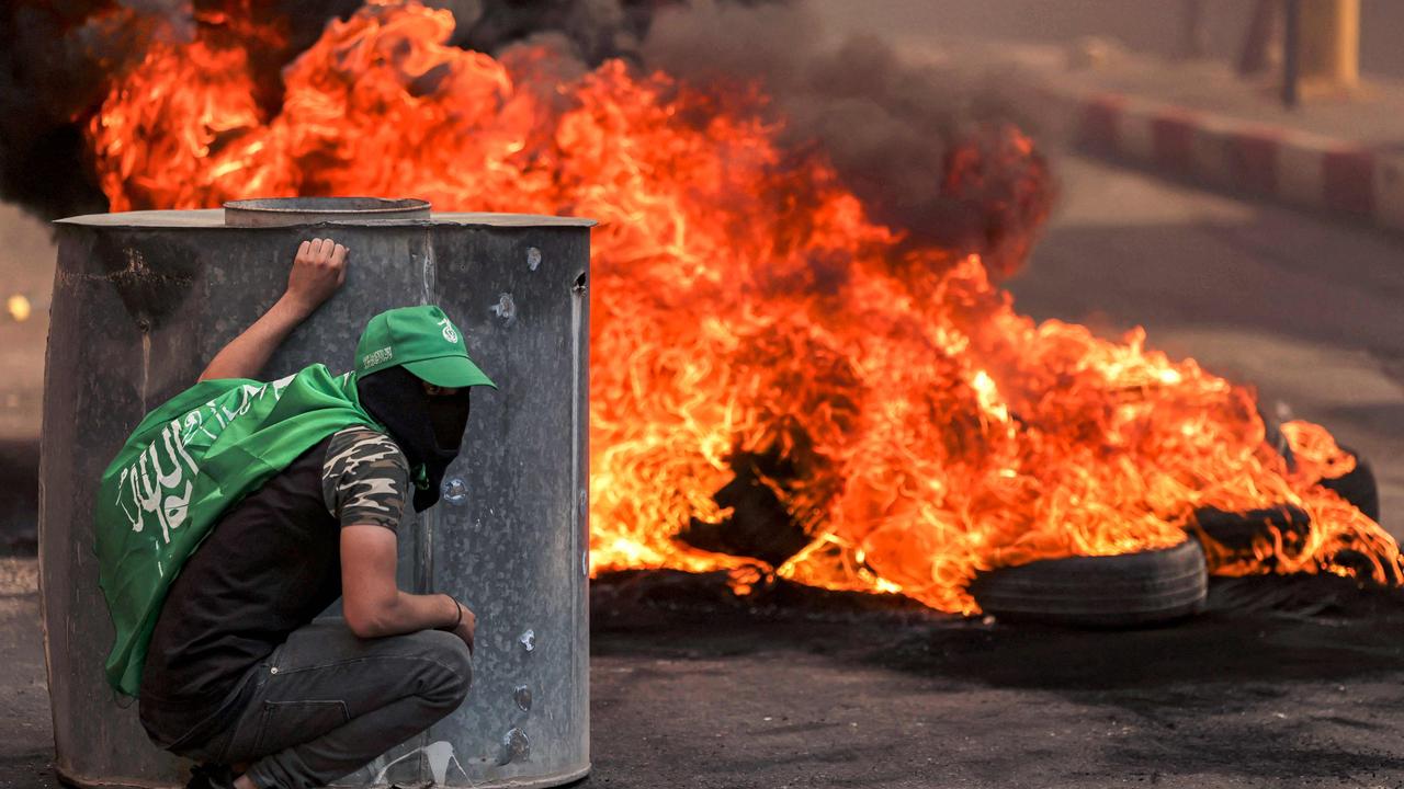 A masked Palestinian protester takes cover near flaming tires during clashes with Israeli forces. Picture: Hazem Bader / AFP