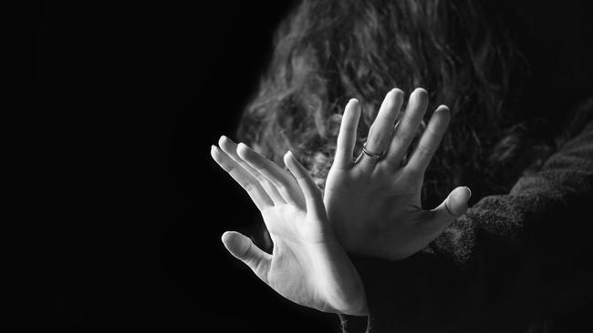 Concept of a violence against women. Black and white portrait of scared and desperate woman, focus on the hands in protective gesture