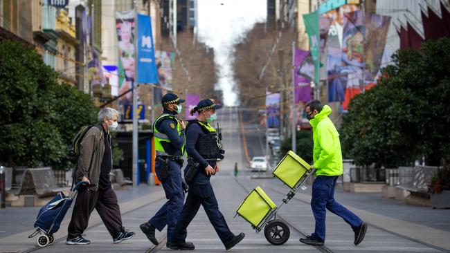 Palice patrol past essential workers and a resident along an eerily quiet Bourke Street during Melbourne’s stage four covid-19 lockdown.. Picture: Mark Stewart