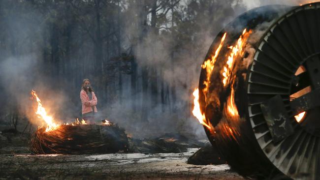 A young girl walks past burning cable spools in Mallacoota. Picture: David Caird