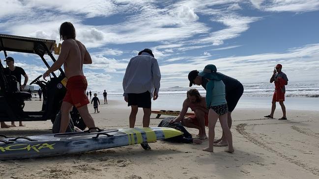 Surf Life Saving Queensland lifeguard Zac Turner pictured on the right assisting a woman who was rescued from dangerous surf with her son on Sunday morning.