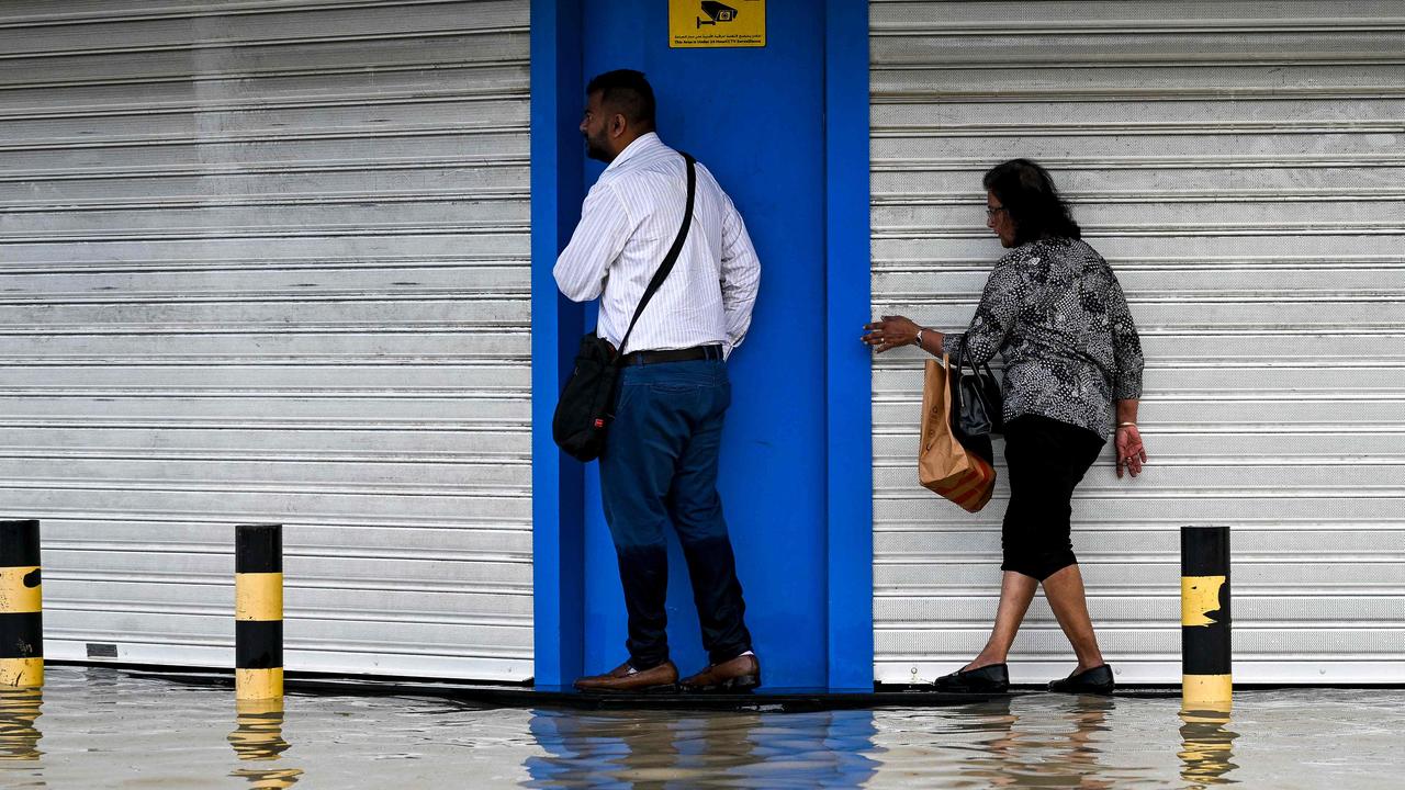 People try to avoid getting wet as they cross a flooded street following heavy rains. (Photo by Ahmed RAMAZAN / AFP)