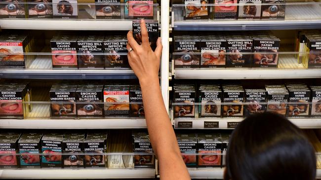 An employee in a Sydney shop adjusts packaged cigarettes which have to be sold in identical olive-brown packets bearing the same typeface and largely covered with graphic health warnings. Picture: William West