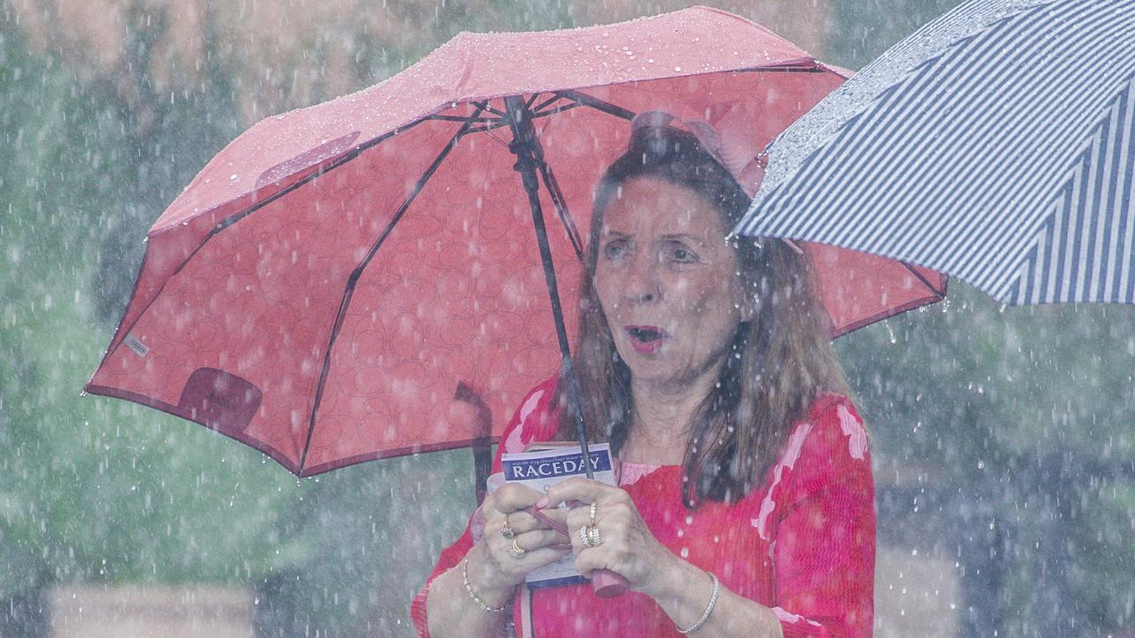 A punter braves heavy showers during the Magic Millions Race Day at Aquis Park. Picture: Glenn Campbell