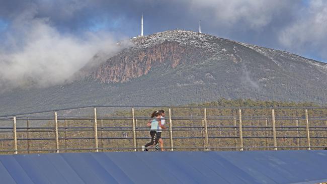 People run along the Bridge of Remembrance at Domain as Kunanyi Mount Wellington is dusted with snow. Picture: Zak Simmonds