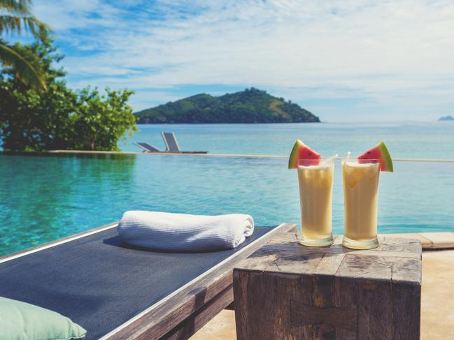 Cocktails by the pool with beach in the background. There are sun lounges with towels. The drinks are Pina coladas with fruit. Copy spacecredit: iStocksaavyescape7 march 2021