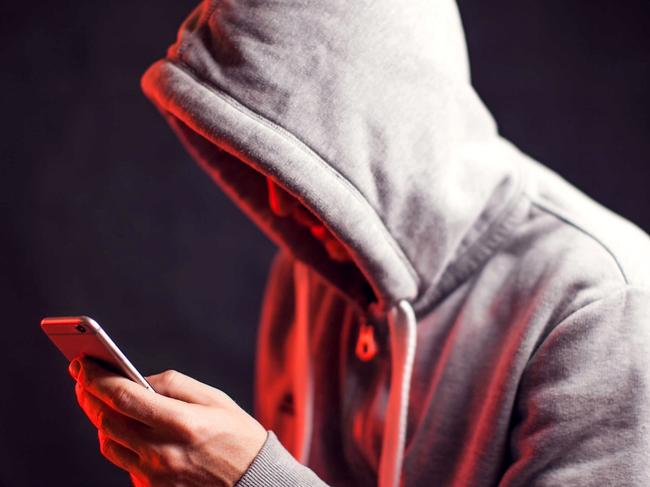 Man wearing hoody sweater with mobile phone in hands. Crime and hacking concept; scam generic.