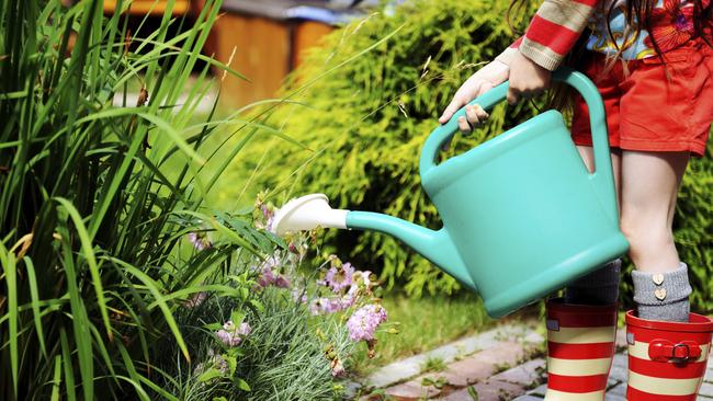 Little girl in a garden with green watering can