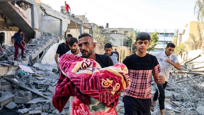 A man carries the remains of an Israeli air strike victim wrapped in a blanket while walking through rubble in Rafah in the southern Gaza Strip. Picture: AFP