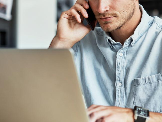 Shot of a young man talking on his cellphone while using his laptop at home