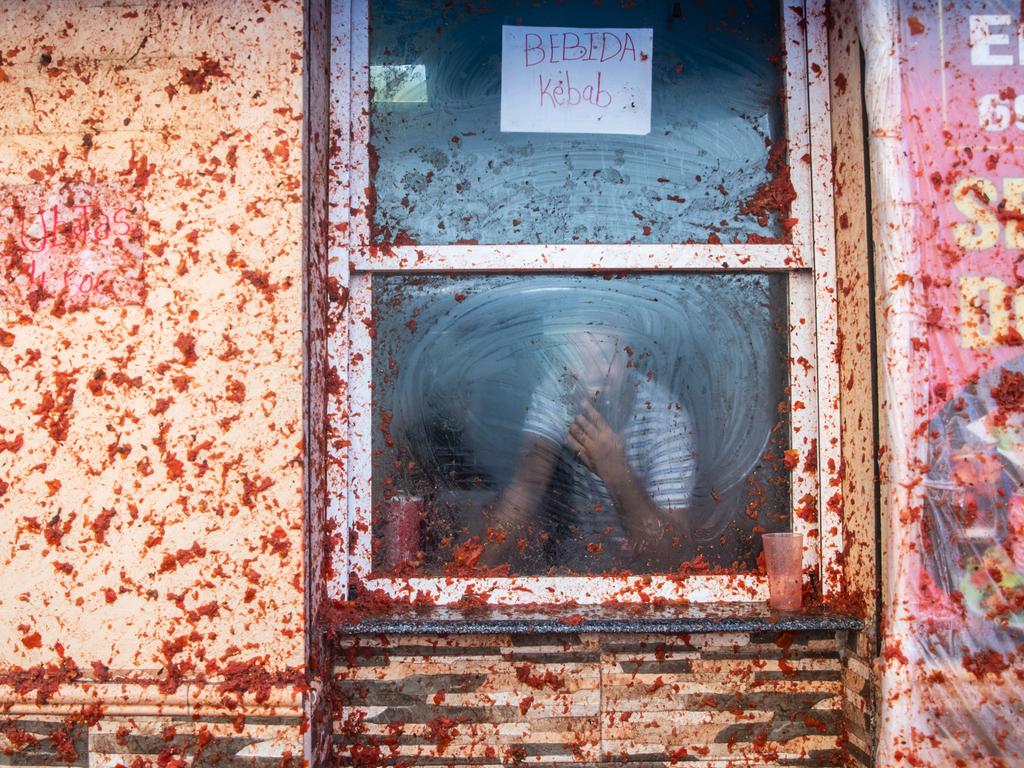 A local business owner watches on from the safety of a closed window while tomato pulp transforms the outer facade of the building. Picture: Zowy Voeten/Getty Images