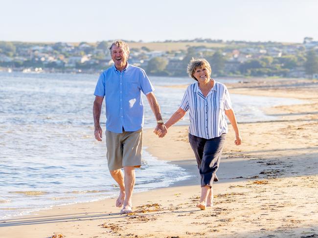 Happy senior couple embracing and holding hands walking on empty beach at sunset. Active healthy elderly woman and man on a romantic walk by the sea. Aging together and retirement lifestyle concept. Middle-aged early retirees generic