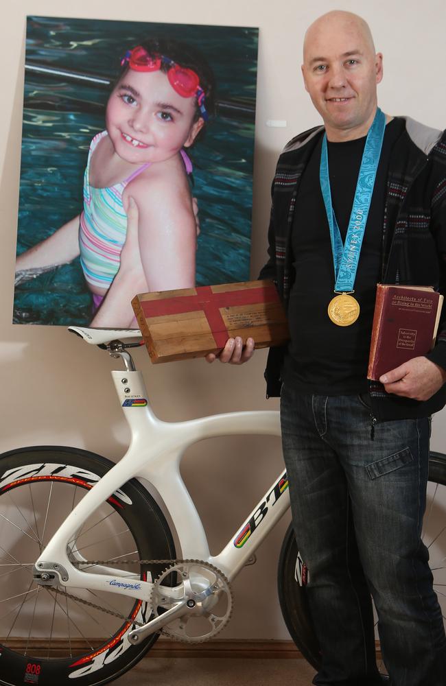 Brett Aitken with five of his favourit things: his favourite photo of his late daughter Ashli, his bike and Olympic gold medal, a 120-year-old book given to him by a close friend, and a piece of the bike track where he created a world record. Picture: Dean Martin