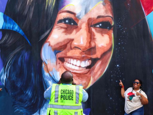 TOPSHOT - A Chicago police officer takes a picture of people posing before a mural of Democratic presidential nominee US Vice President Kamala Harris outside the United Center ahead of the Democratic National Convention (DNC) in Chicago, Illinois on August 17, 2024. The mural, created by Ian Robertson and Salt and Pique Brown, was commissioned by Emilyâs List in 2020. Vice President Kamala Harris will formally accept the partyâs nomination for president at the DNC which runs from August 19-22 in Chicago. (Photo by Charly TRIBALLEAU / AFP)