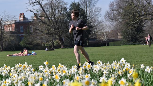 A jogger runs past people enjoying the sunshine and daffodils in Greenwich Park, London. Who has the right approach? Picture: AFP