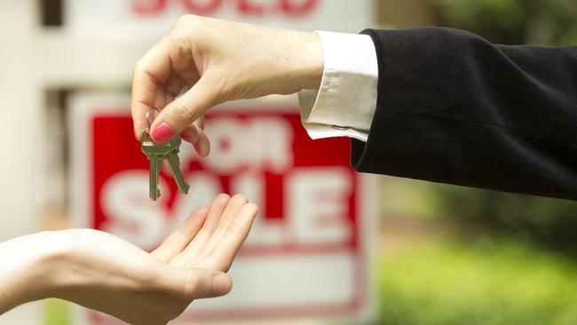 iStock photo of agent handing over keys in front of a for sale / sold sign. For On the Pulse column in Cairns Post weekend real estate liftout.