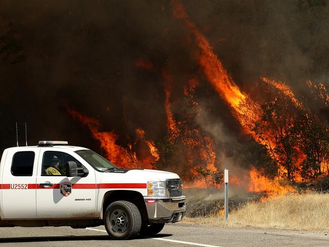 Cal Fire firefighters pass by a wall of flames as the Carr Fire burns trees along highway 299 on July 27, 2018 near Whiskeytown, California. Picture: Getty