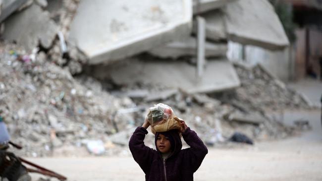 A girl carrying a bag of bread walks past a building destroyed during Israeli strikes at the Nusseirat refugee camp, on March 20, 2025. Picture: Eyad Baba / AFP