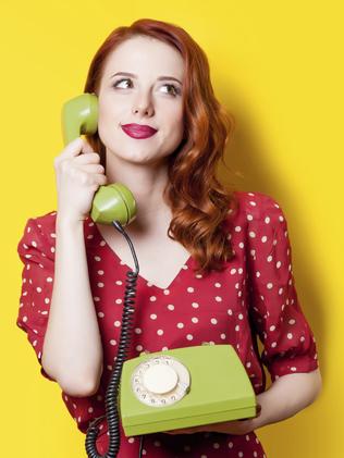 Smiling redhead girl in red polka dot dress with green dial phone on yellow background.