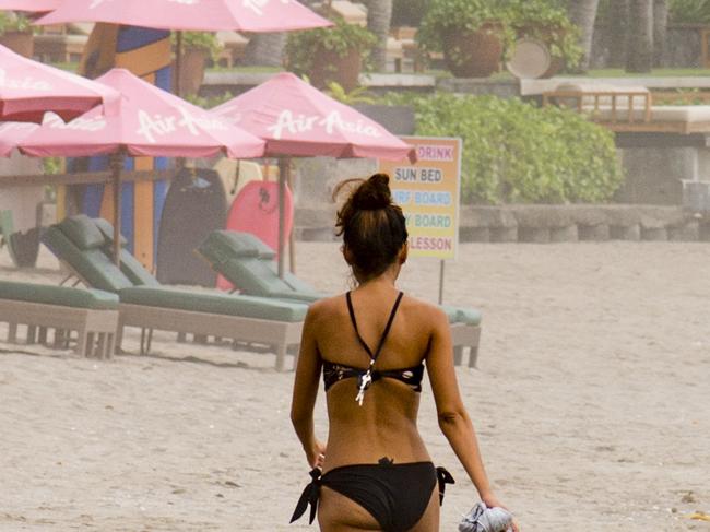 Beautiful lady walking on the beach of Seminyak, Bali, Indonesia, during a cloudy day.