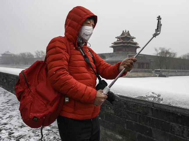 A Chinese man wears a protective mask as he takes photos during a snowfall outside the closed Forbidden City in Beijing. Picture: Getty Images