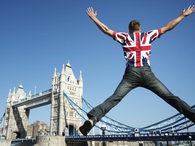 Man in Union Jack (UK flag) t-shirt jumping in front of bright view of London skyline at Tower Bridge