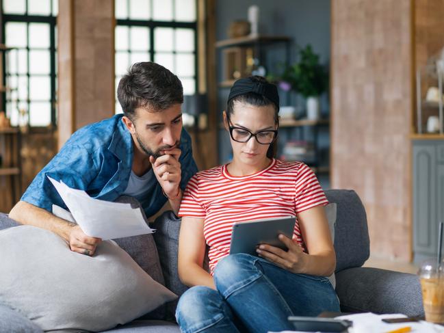 Couple calculating bills at home using laptop and calculator. Young couple working on computer while calculating finances sitting on couch. Young  man with  wife at home analyzing their finance with documents.