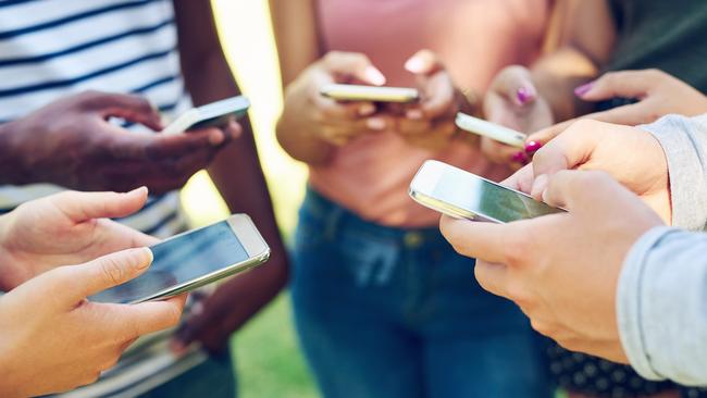 A group of friends using their phones together outdoors.