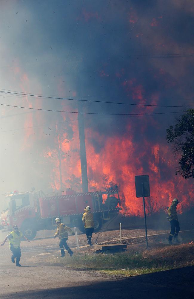 Fireys and police run for it as an out of control bushfire jumps Wine Country Drive and smashes head on into the village of North Rothbury, north of Cessnock on Tuesday. Picture: Peter Lorimer