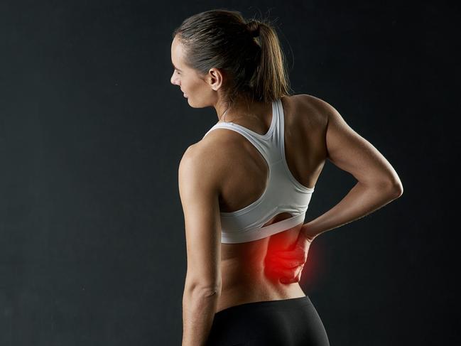 Studio shot of a sporty young woman holding her lower back in pain against a dark background