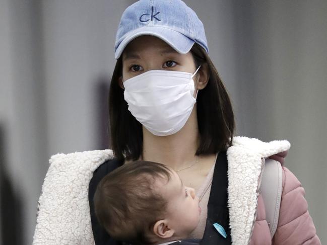 A woman wears a protective mask as she holds a baby while she walks through in terminal 5 at O'Hare International Airport in Chicago, Sunday, March 1, 2020. (AP Photo/Nam Y. Huh)